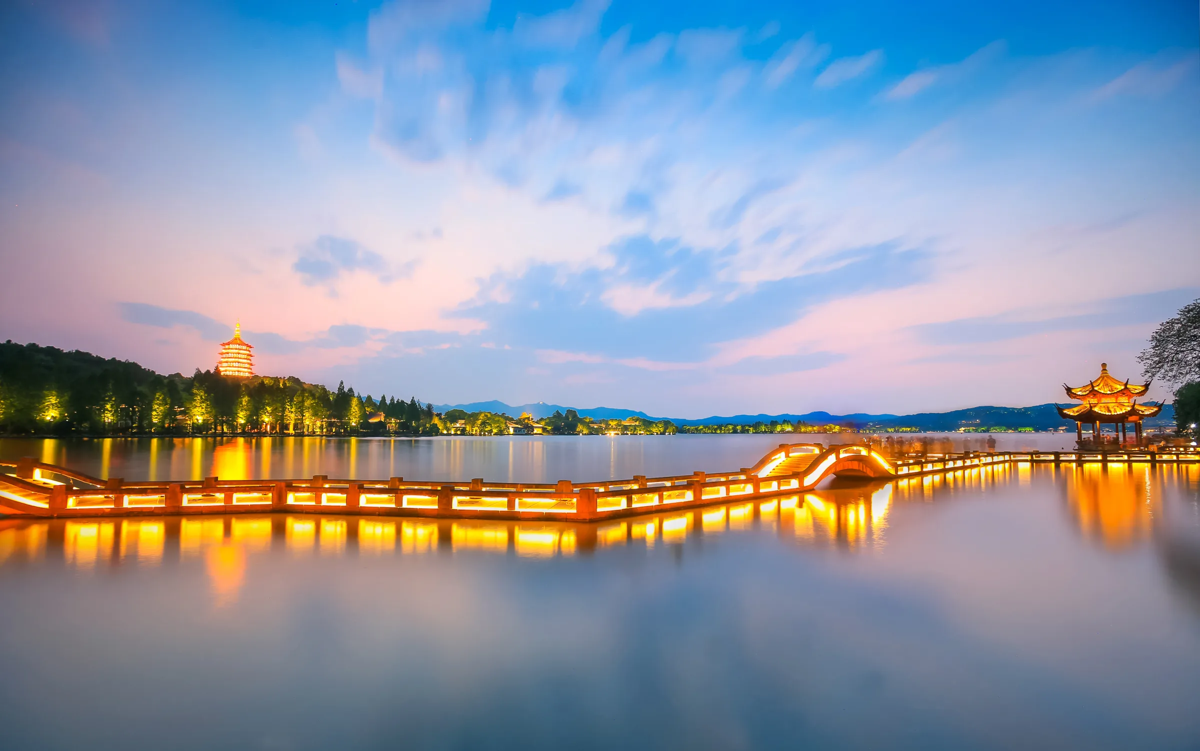 West Lake at blue hour with Leifeng Pagoda, a lit causeway, pavilion and dark wooded hills