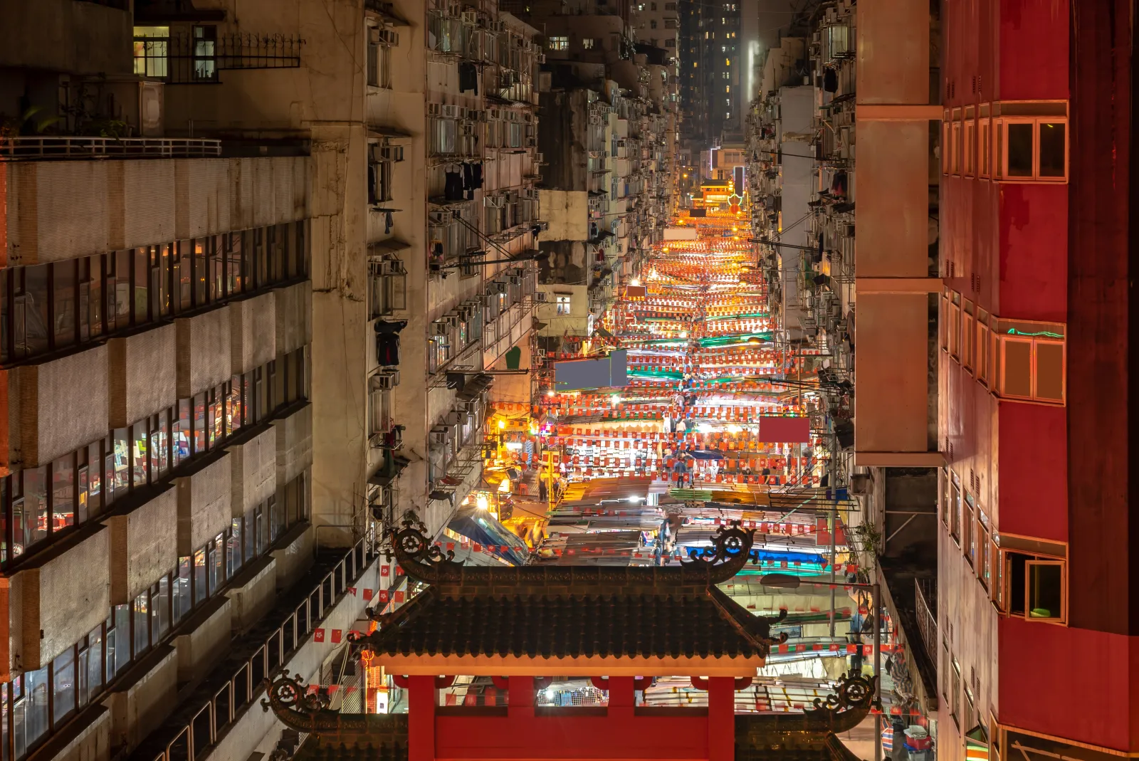 Temple Street Night Market glowing between dense residential buildings in Hong Kong at night