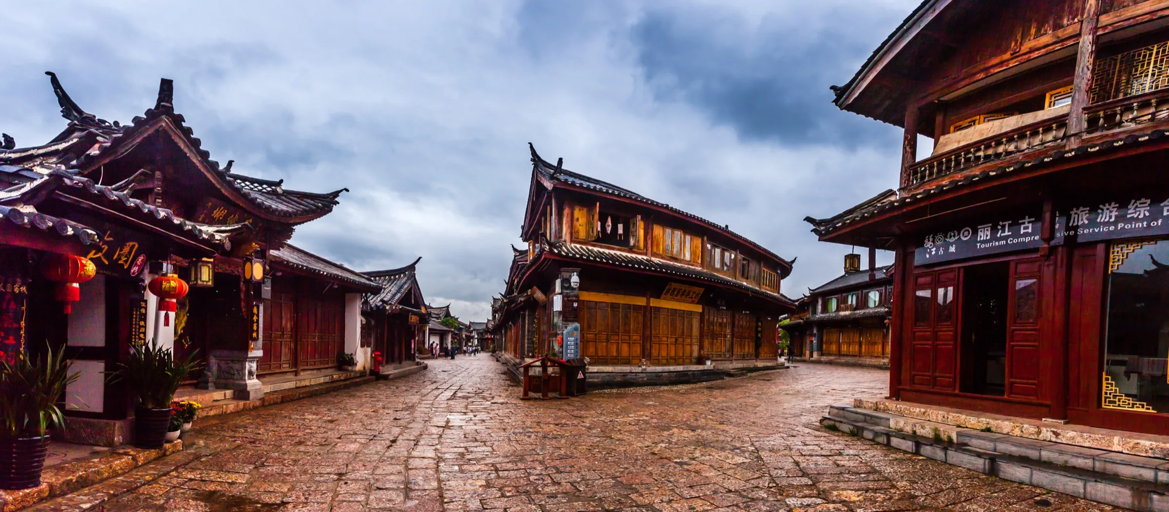Rain-darkened stone lanes and timber buildings beneath a cloudy sky in Lijiang Old Town