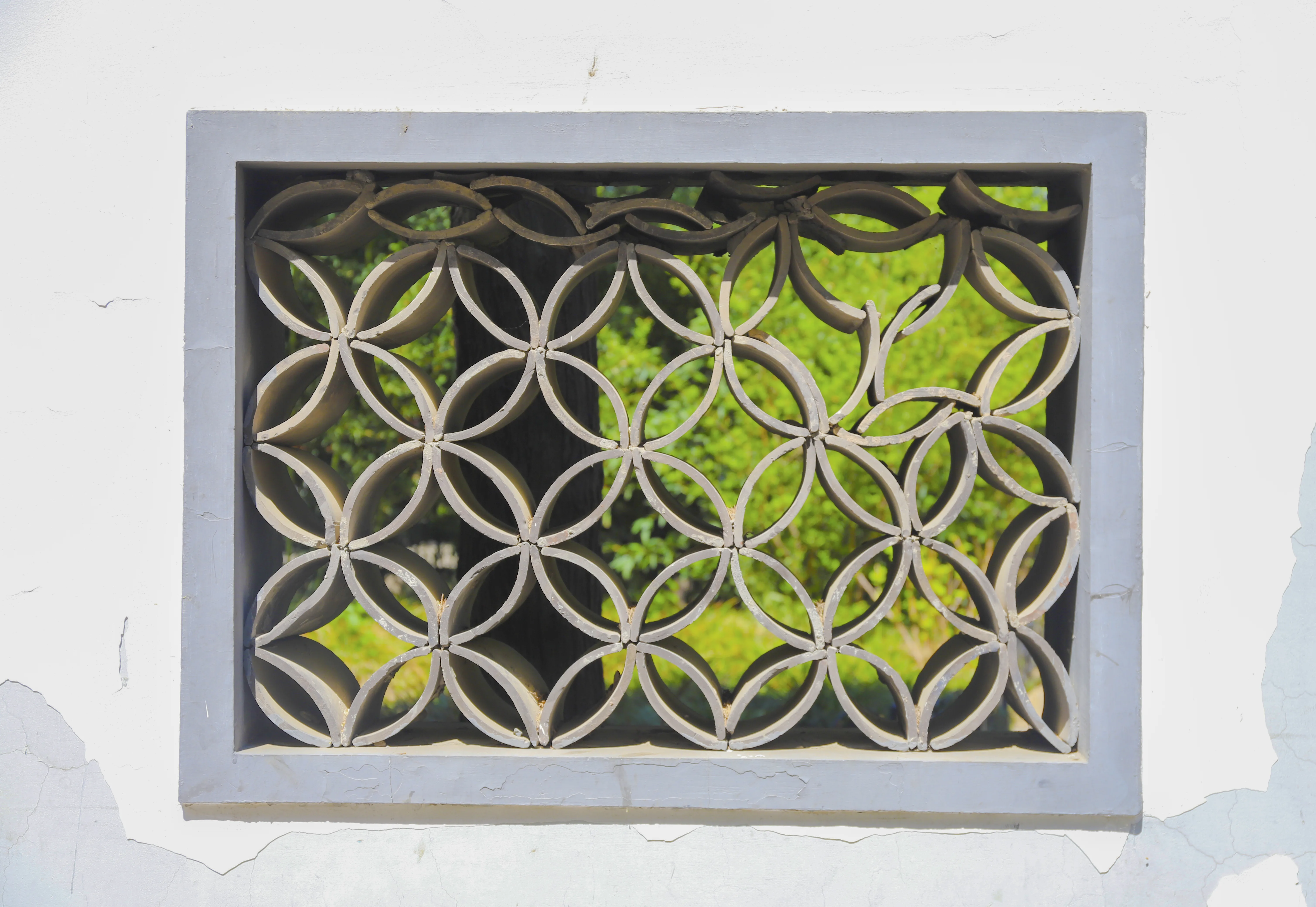 A geometric lattice window in a white Suzhou garden wall framing green plants beyond it