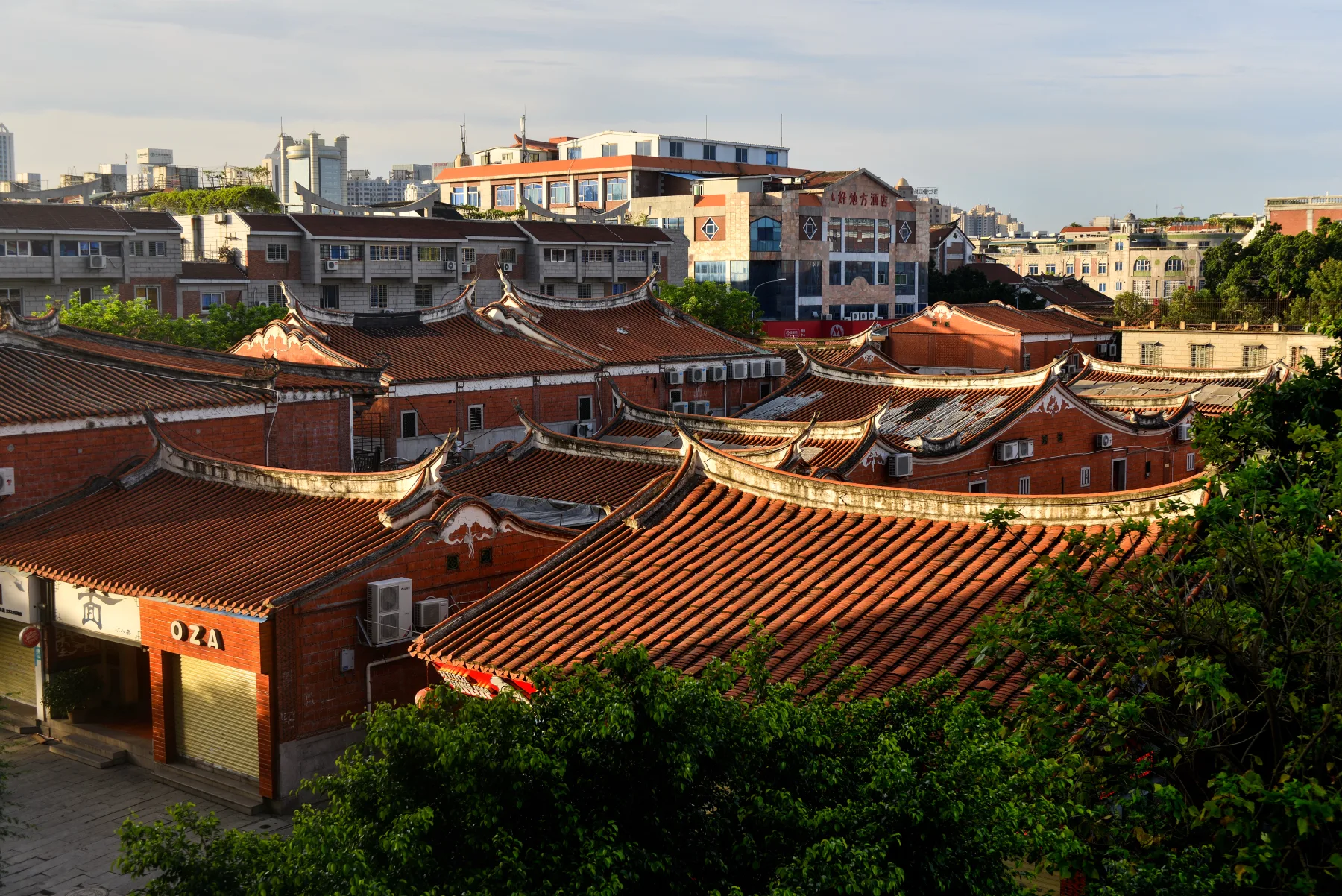 Layered red-tile Minnan roofs in Quanzhou old city with modern buildings behind them